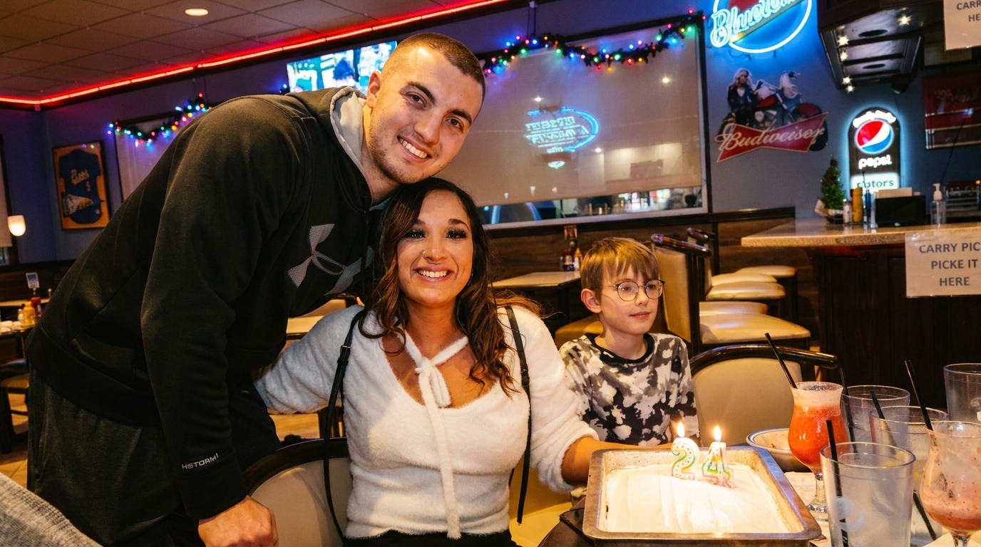 A family celebrates a birthday with cake and drinks at a restaurant with neon signs.