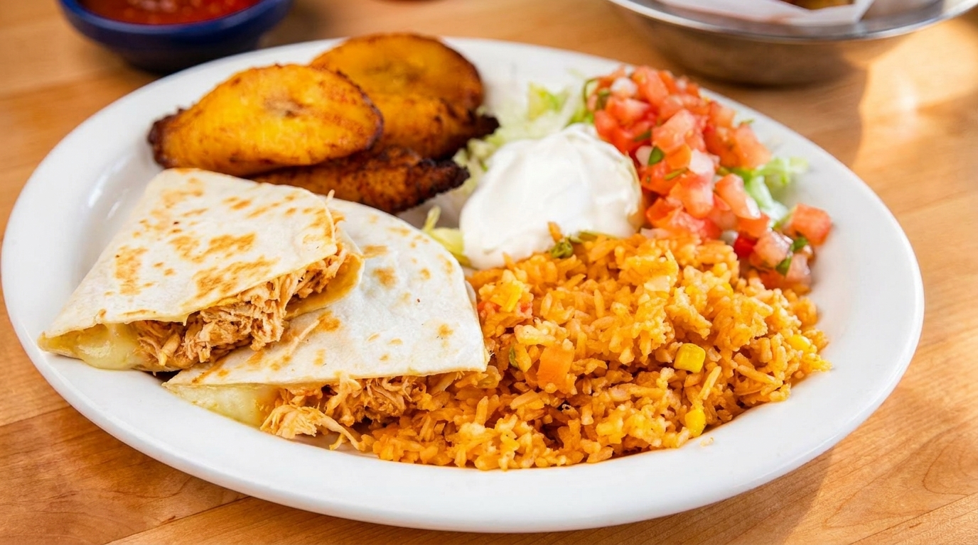 A white plate with chicken quesadillas, yellow rice, fried plantains, sour cream, and pico de gallo.