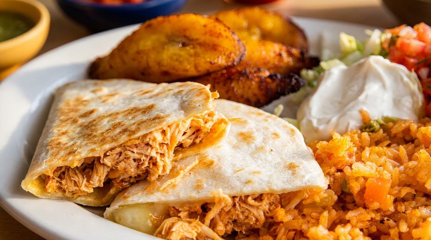 Chicken quesadilla with rice, plantains, sour cream, and pico de gallo on a white plate.