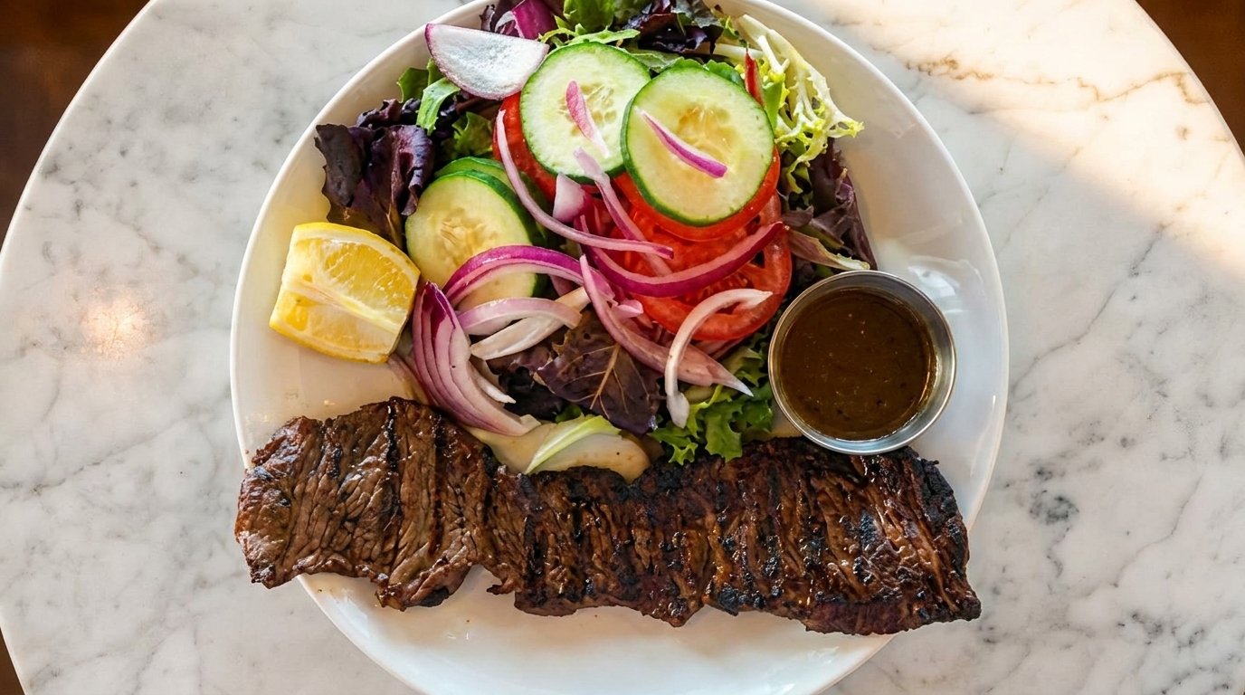 Grilled steak with a side salad of mixed greens, cucumbers, tomatoes, red onions, and a lemon wedge.
