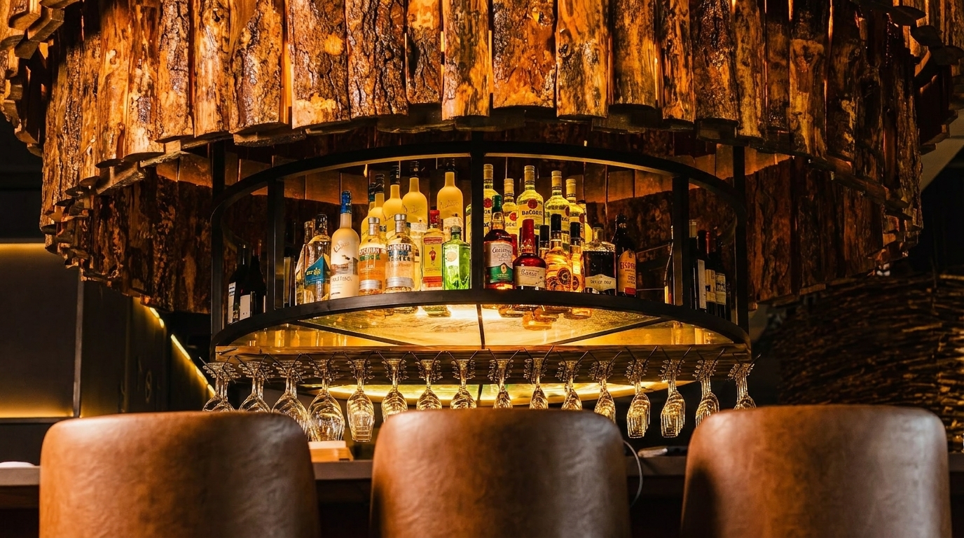 A rustic bar with a wooden chandelier, liquor bottles, hanging glasses, and bar stools.