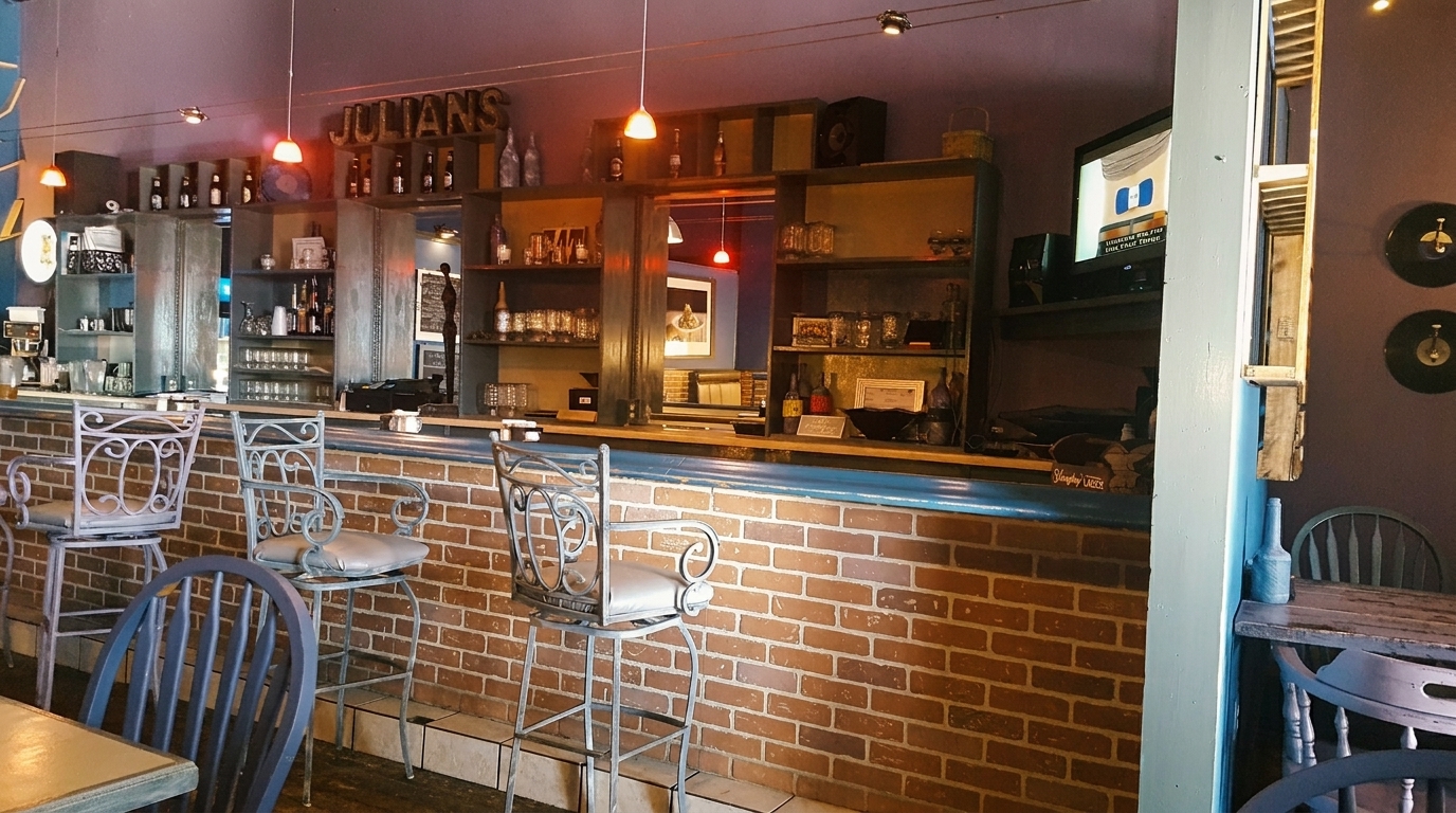 A bar area with a brick facade, bar stools, shelves with bottles and glasses, and a TV.