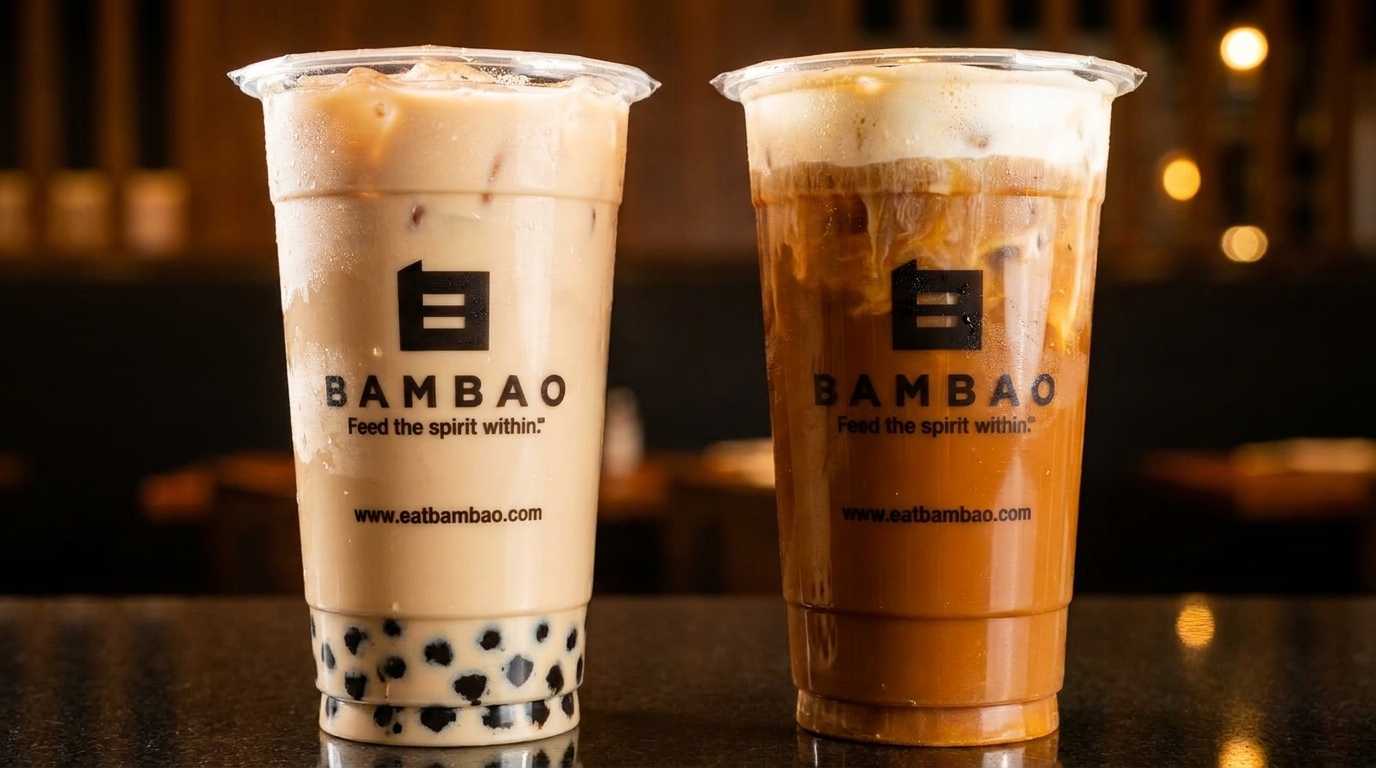 Two Bambao drinks, one light-colored with boba and one dark-colored with foam, on a dark surface.