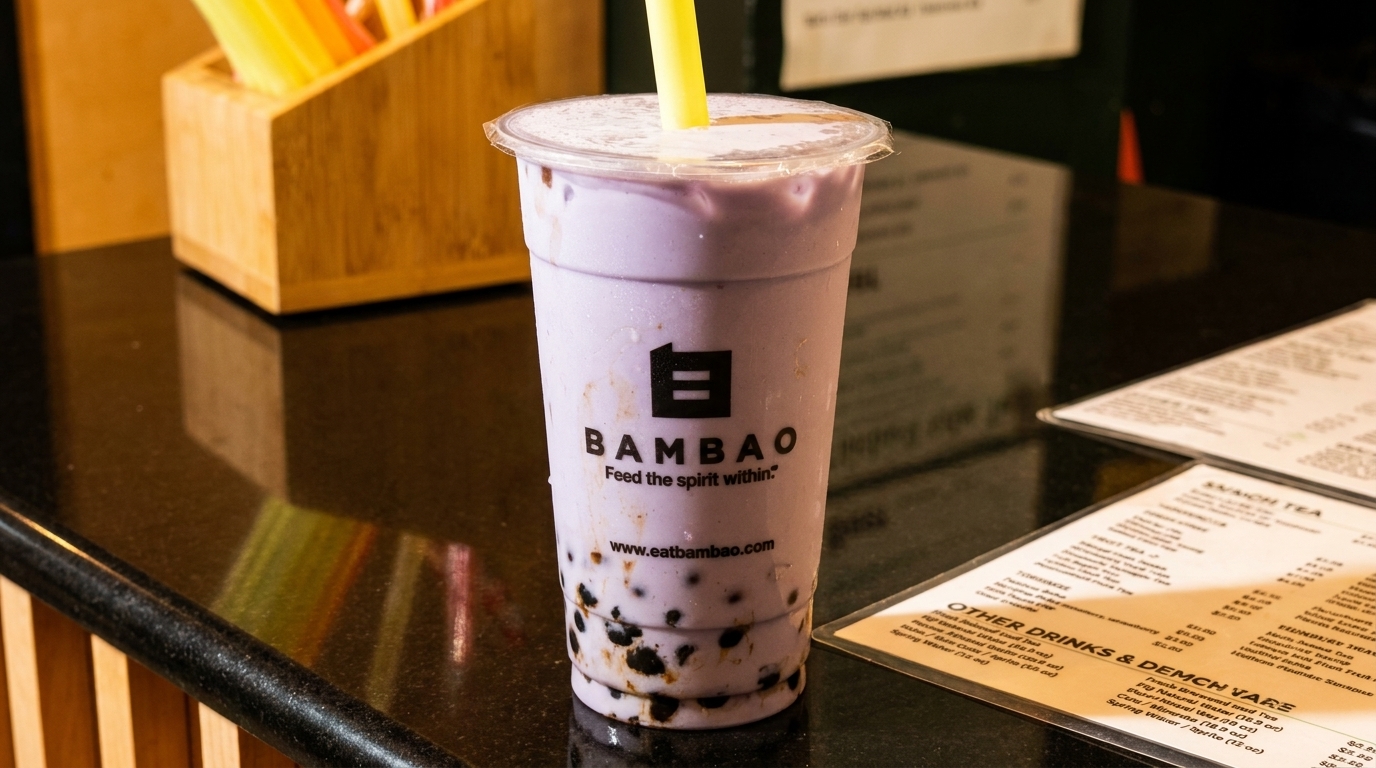 A purple taro bubble tea with a yellow straw and the Bambao logo sits on a black counter.