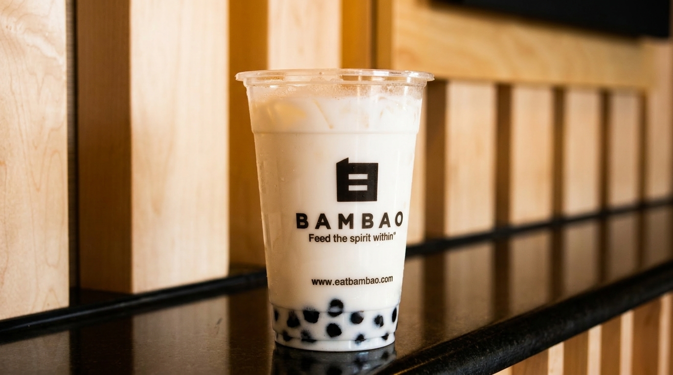 A BambaO bubble tea with tapioca pearls sits on a reflective black counter against a wooden wall.