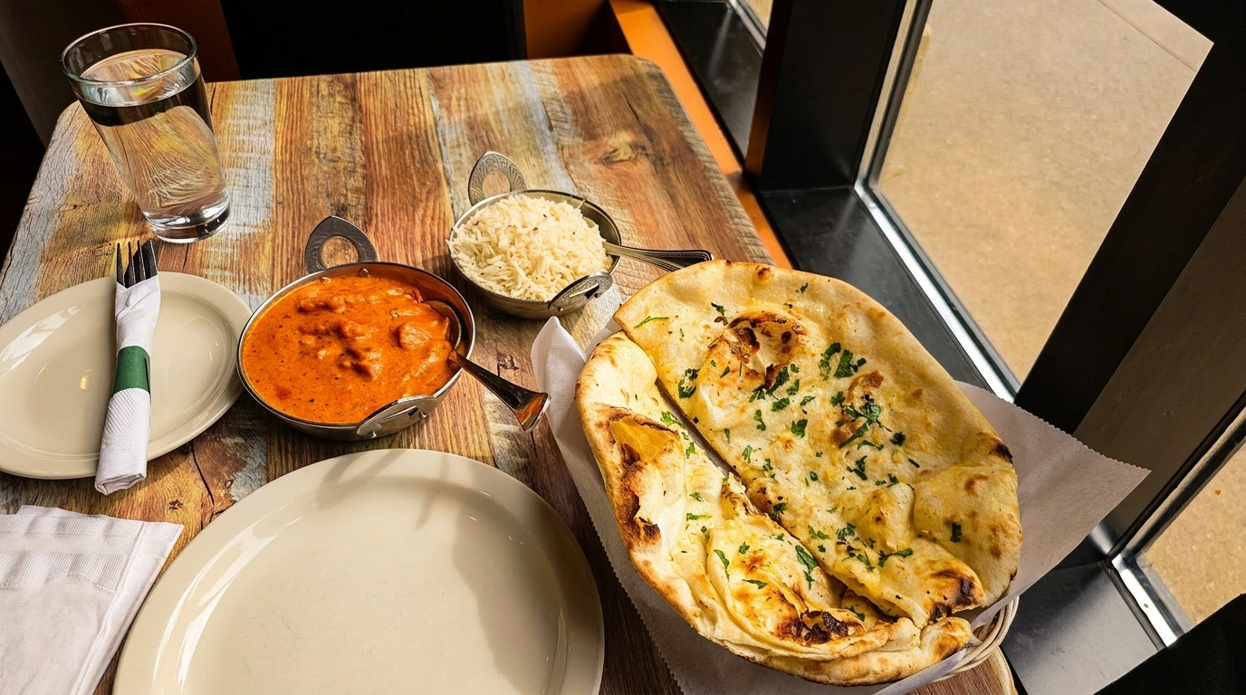 Indian meal with butter chicken, rice, and naan bread on a rustic wooden table.