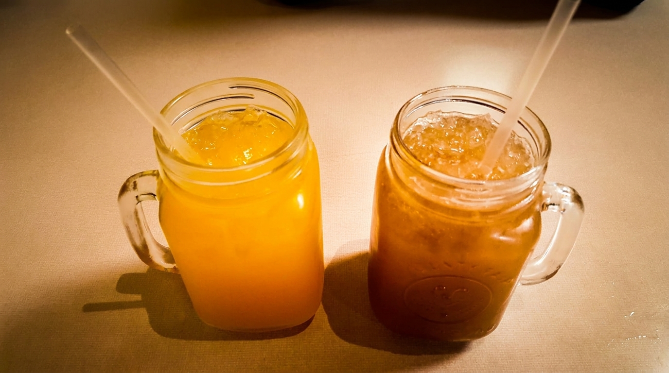 Two mason jar mugs filled with iced drinks, one orange and one brown, with straws.
