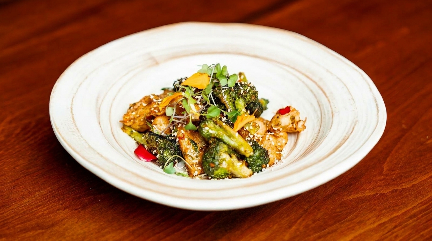 Chicken and broccoli stir-fry with sesame seeds and microgreens in a white bowl on a wooden table.