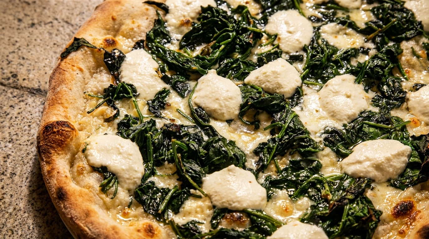 Close-up of a white pizza with spinach and dollops of ricotta cheese on a stone surface.