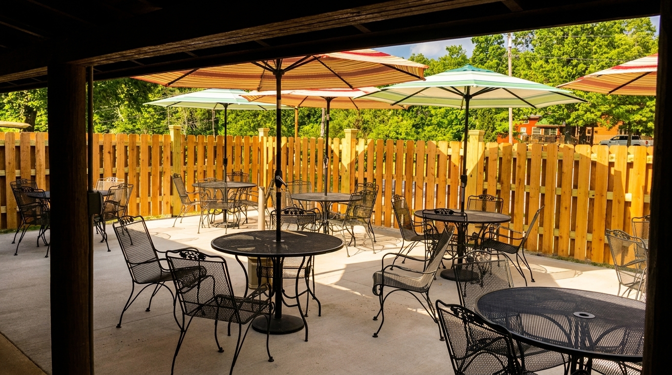 Outdoor patio with black metal tables and chairs, striped umbrellas, and a wooden fence.
