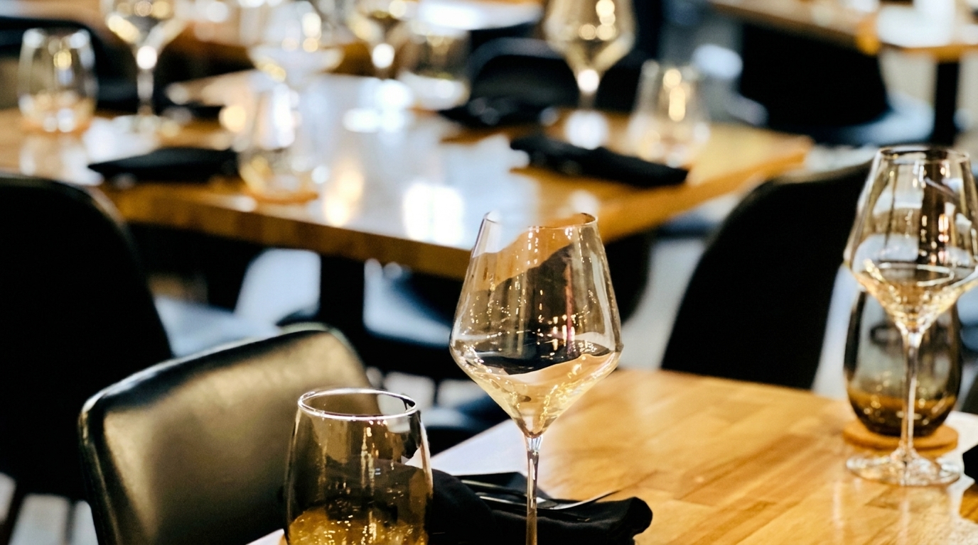 Wine glasses and place settings on wooden tables in a dimly lit restaurant dining room.