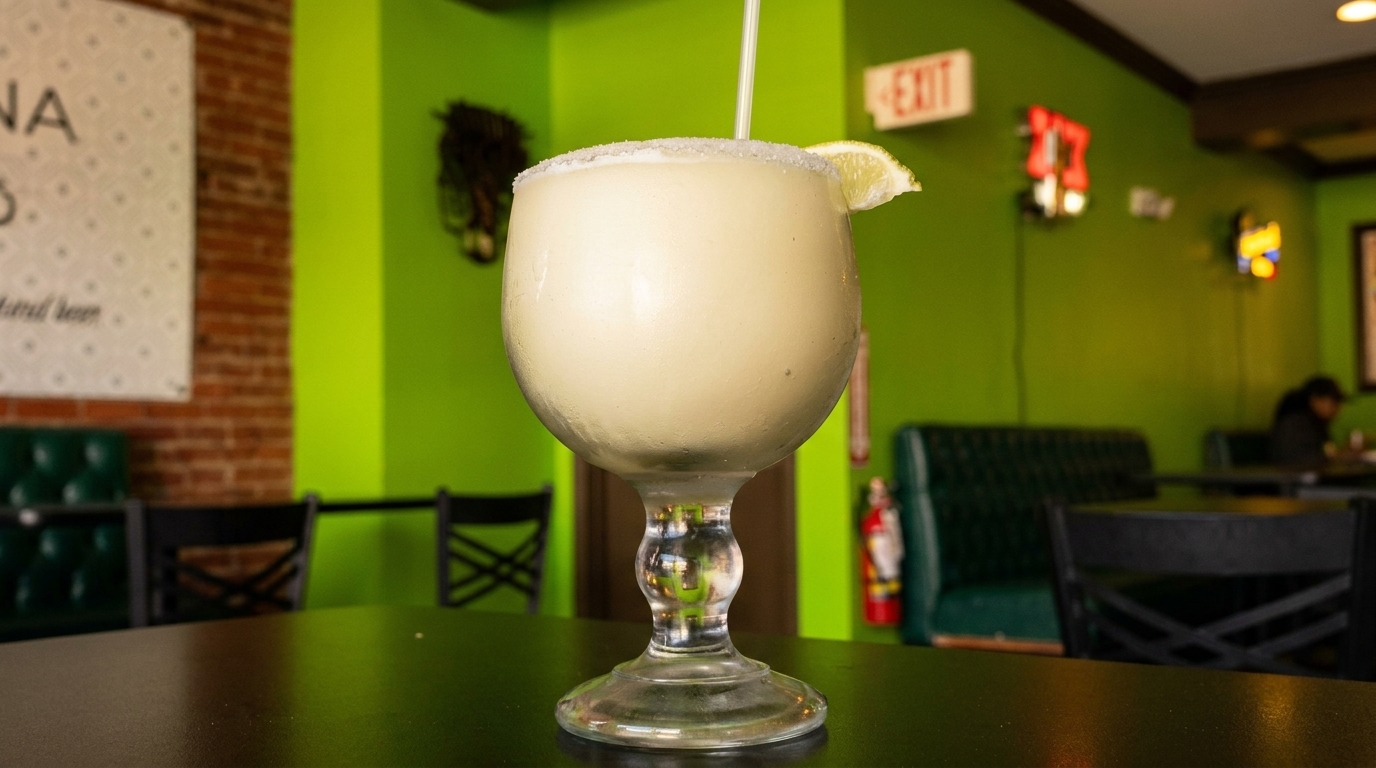 A frozen margarita with a salted rim and lime wedge sits on a table in a vibrant green restaurant.