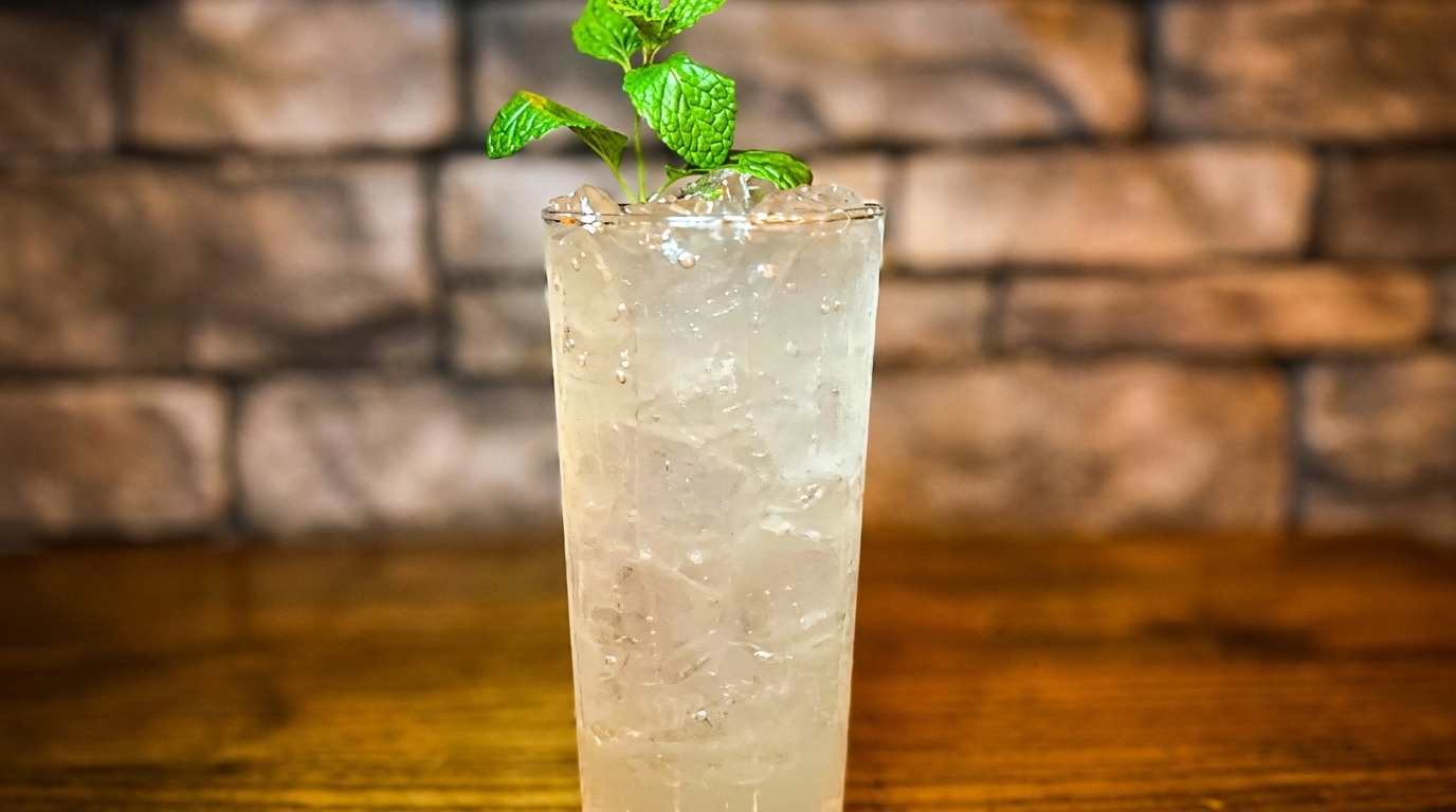 A tall glass of iced lemonade garnished with fresh mint, on a wooden table with a brick wall background.