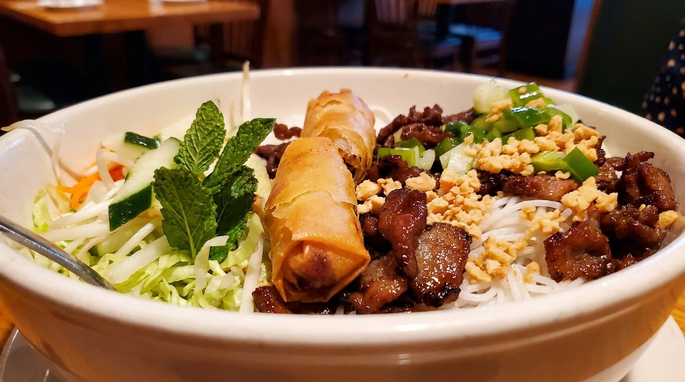 A close-up of a Vietnamese vermicelli bowl with grilled pork, spring rolls, and fresh vegetables.
