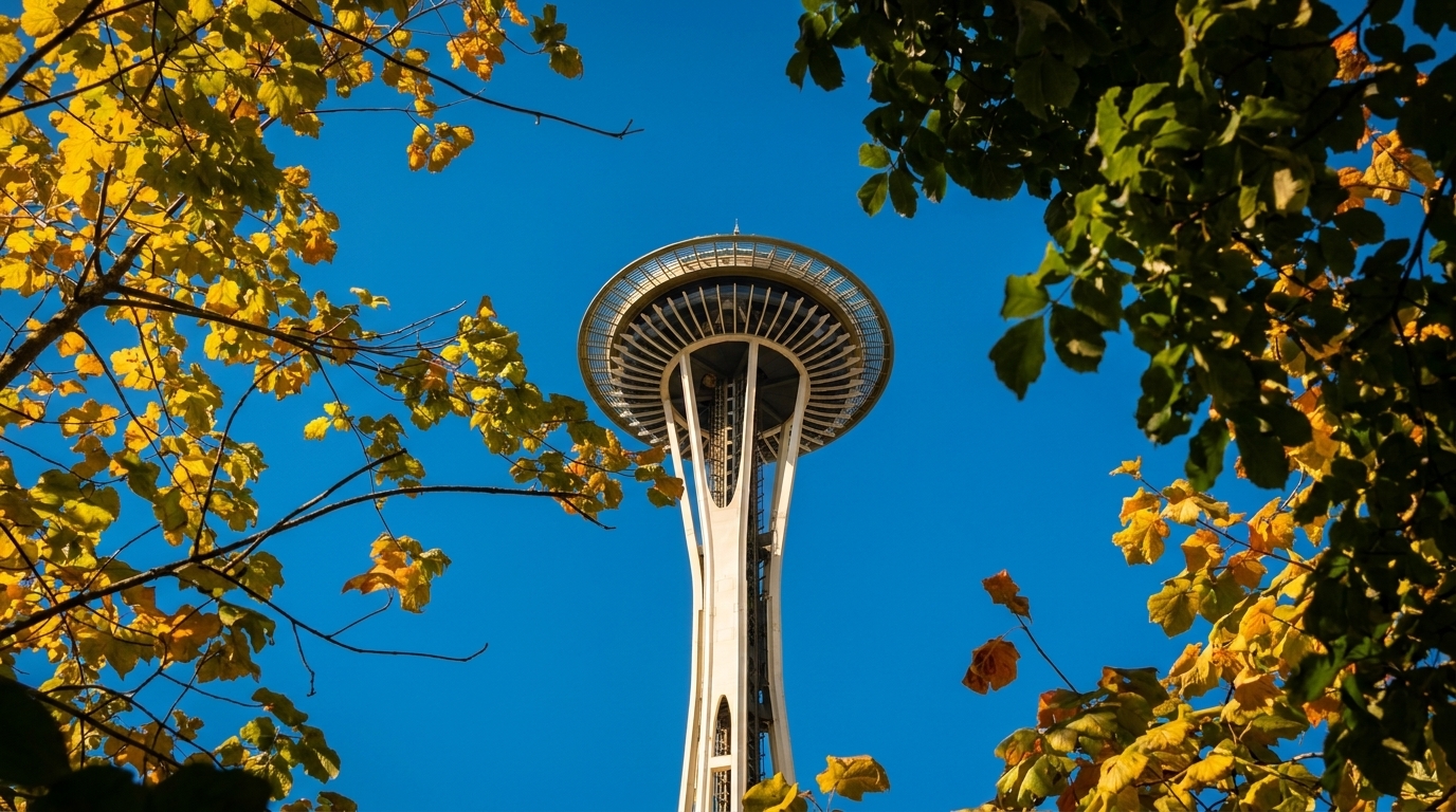 The Seattle Space Needle rises against a clear blue sky, framed by autumn leaves.