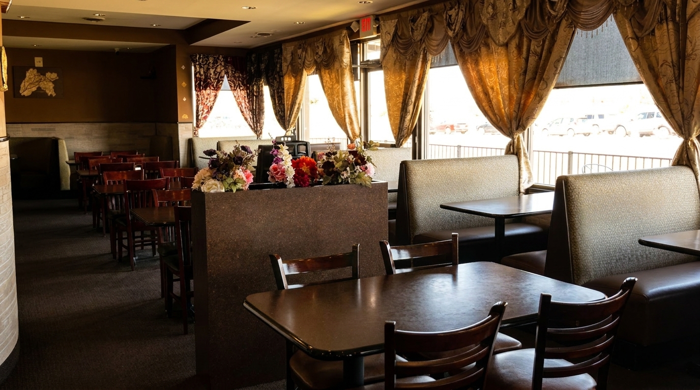 Empty restaurant dining room with dark wood tables, upholstered booths, and ornate golden curtains.