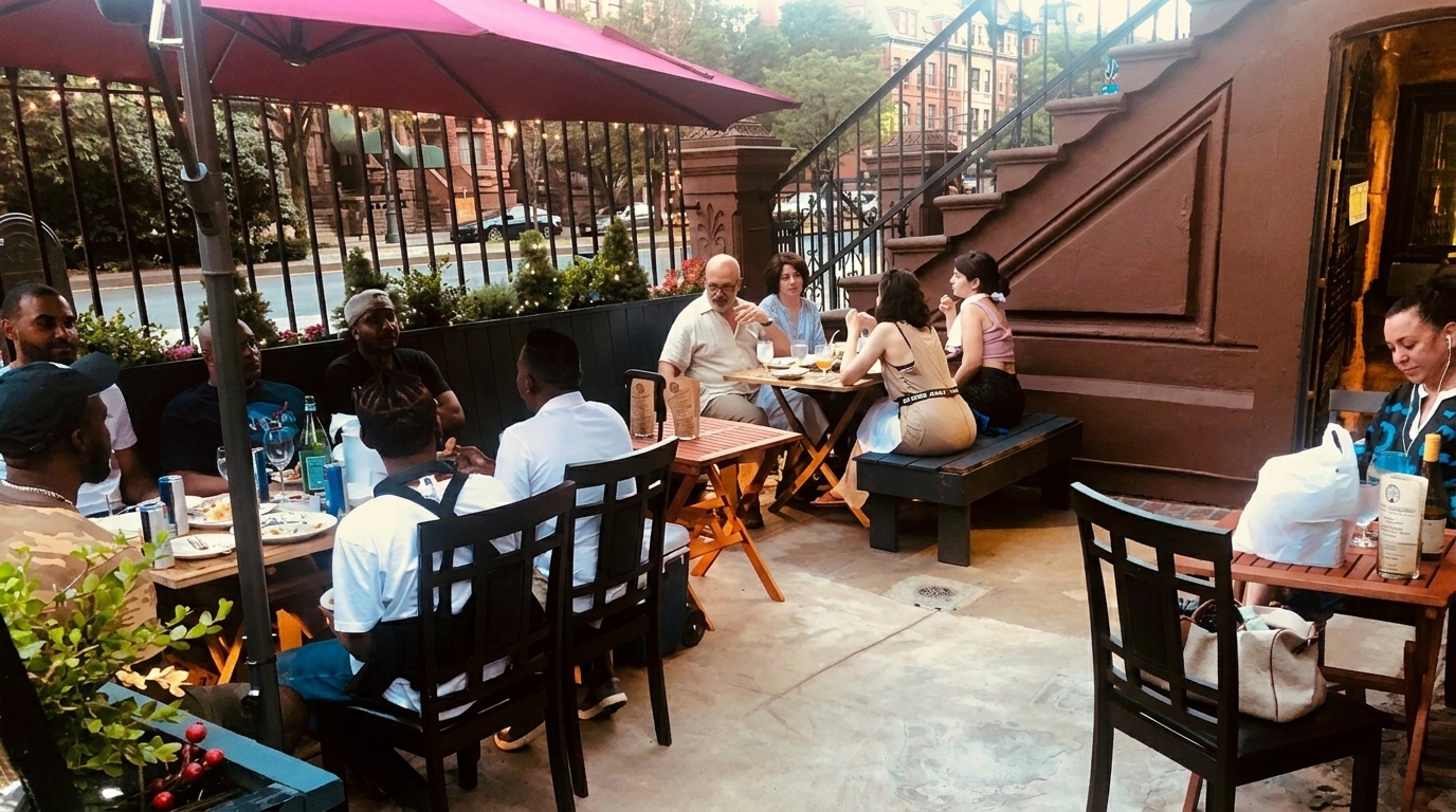 Patrons enjoying food and drinks at outdoor tables under a pink umbrella on a restaurant patio.