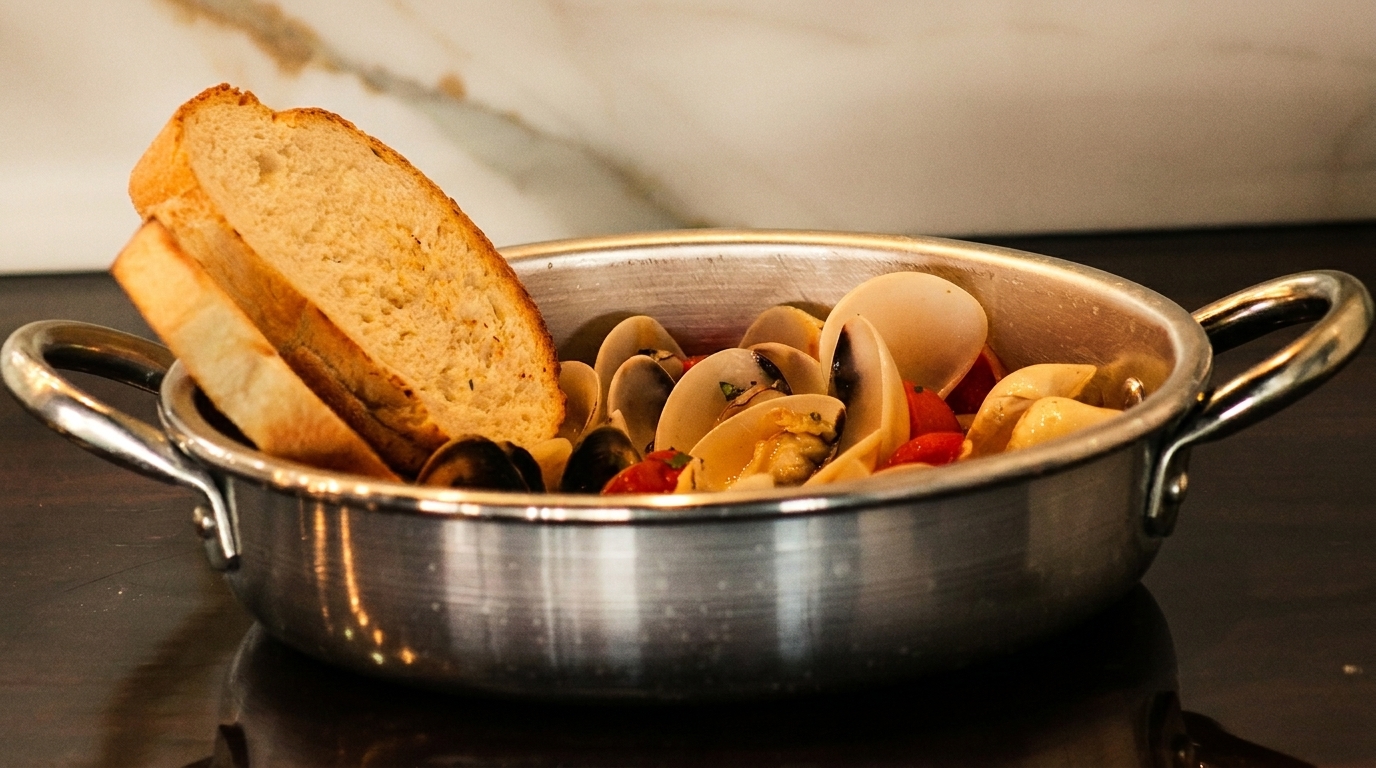 Steamed clams with cherry tomatoes and two slices of toasted bread in a metal pot.
