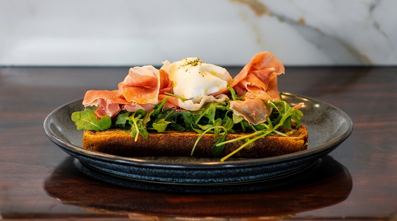Toasted bread topped with prosciutto, arugula, and a poached egg on a dark plate.