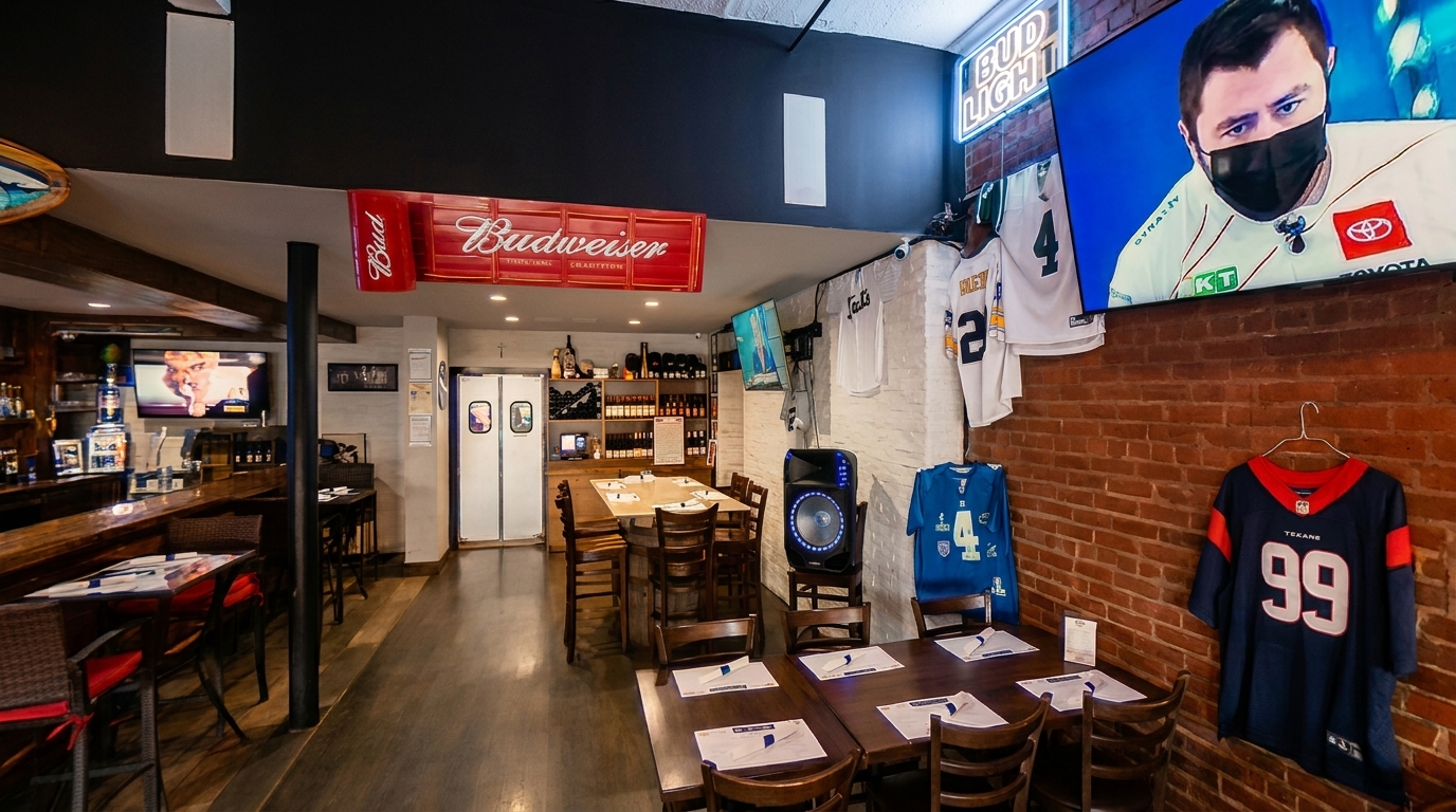 A sports bar interior with a long wooden bar, dining tables, and sports jerseys on brick walls.