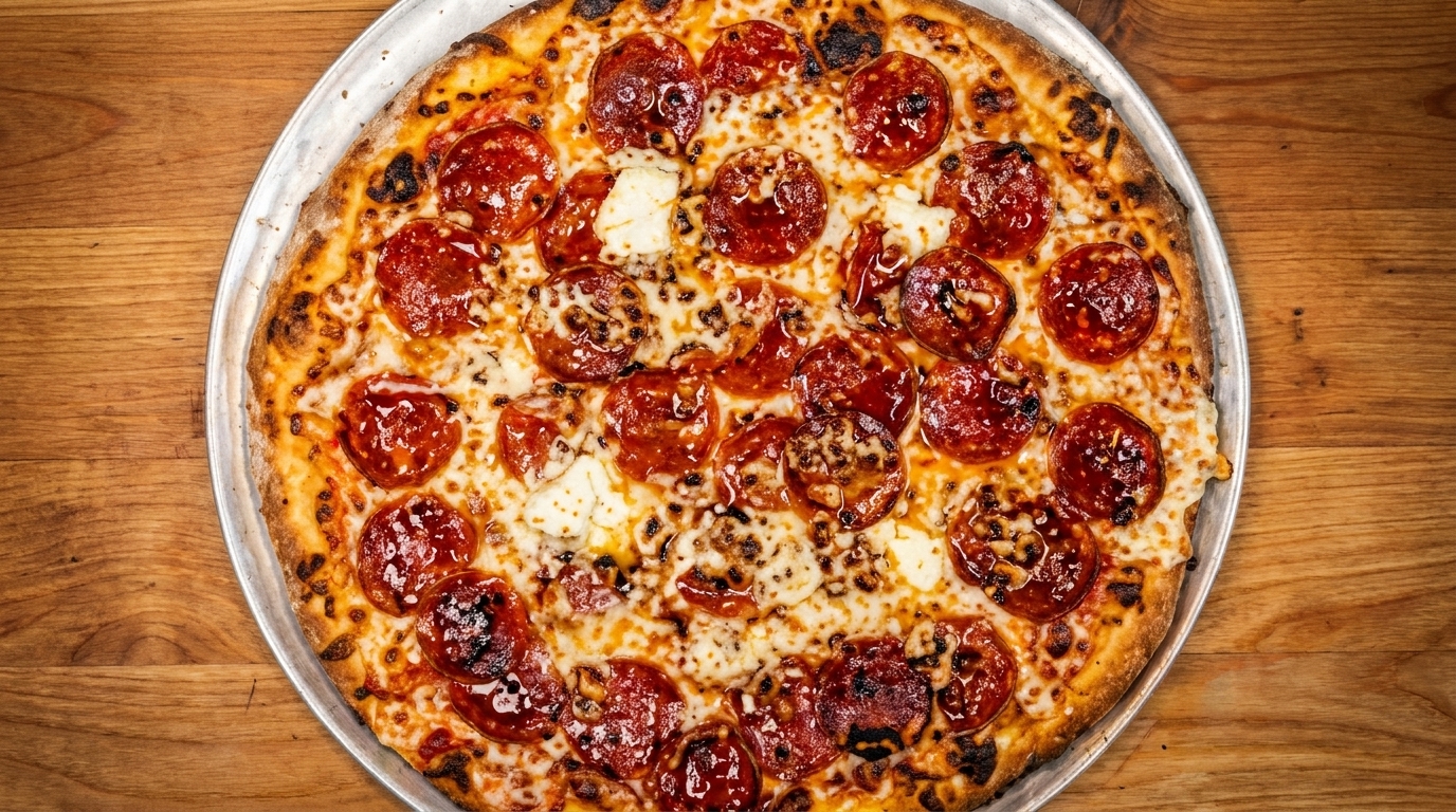 A whole pepperoni and cheese pizza on a metal pan, centered on a wooden table.