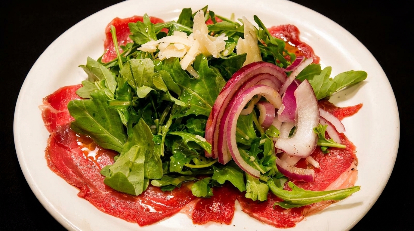 Carpaccio with arugula, shaved Parmesan, and red onion on a white plate.