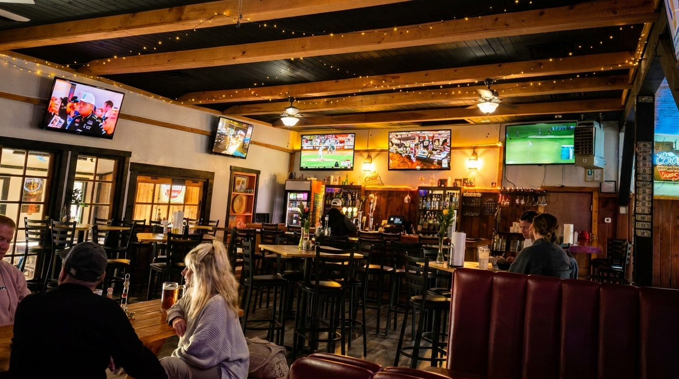 A lively bar interior with multiple TVs showing sports, patrons at tables, and a bartender.