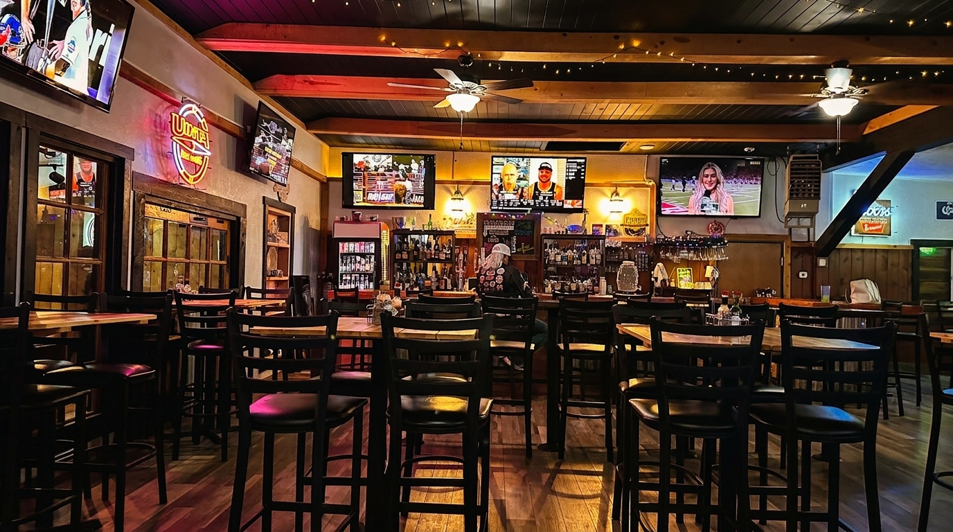 A dimly lit bar interior with high-top tables, chairs, multiple TVs, and a well-stocked bar.