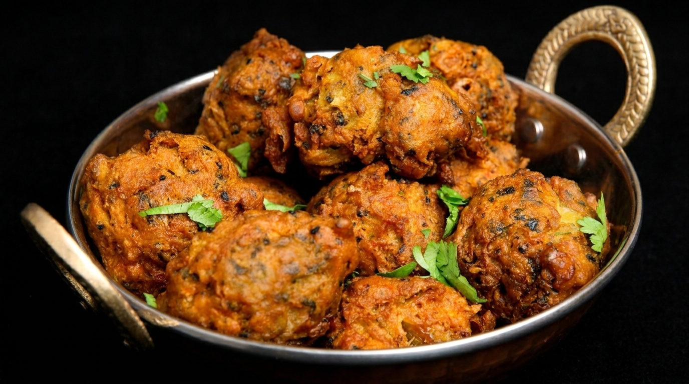 Golden-brown pakoras, garnished with fresh cilantro, served in a traditional copper bowl.