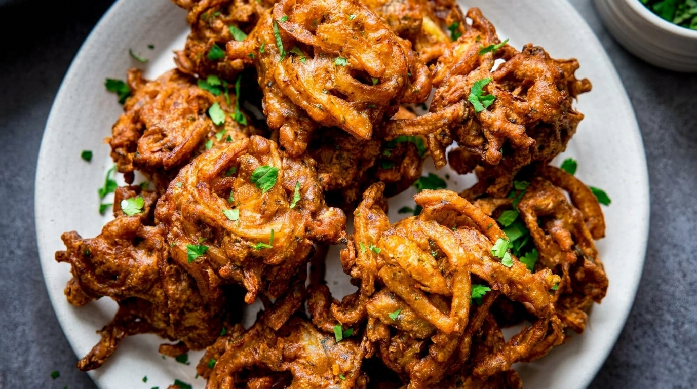 Crispy golden-brown onion bhaji fritters, garnished with fresh green cilantro, on a white plate.