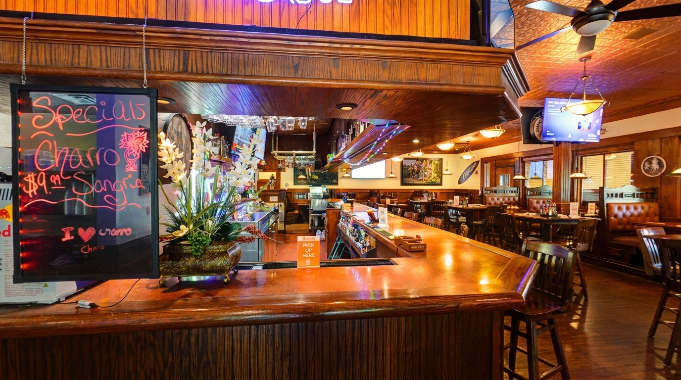 Warmly lit restaurant interior with a wooden bar, dining tables, booths, and a specials sign.