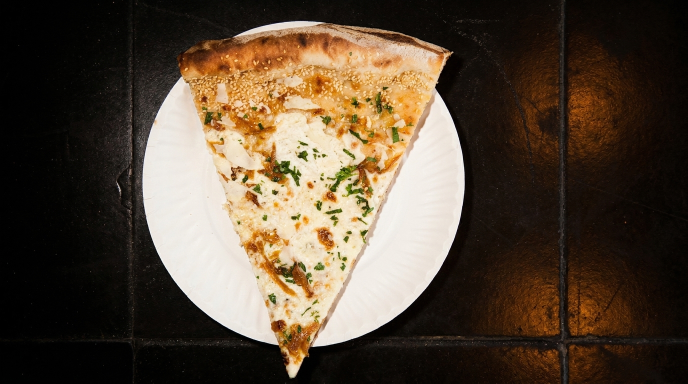 A slice of white pizza with caramelized onions, cheese, and parsley on a white paper plate.