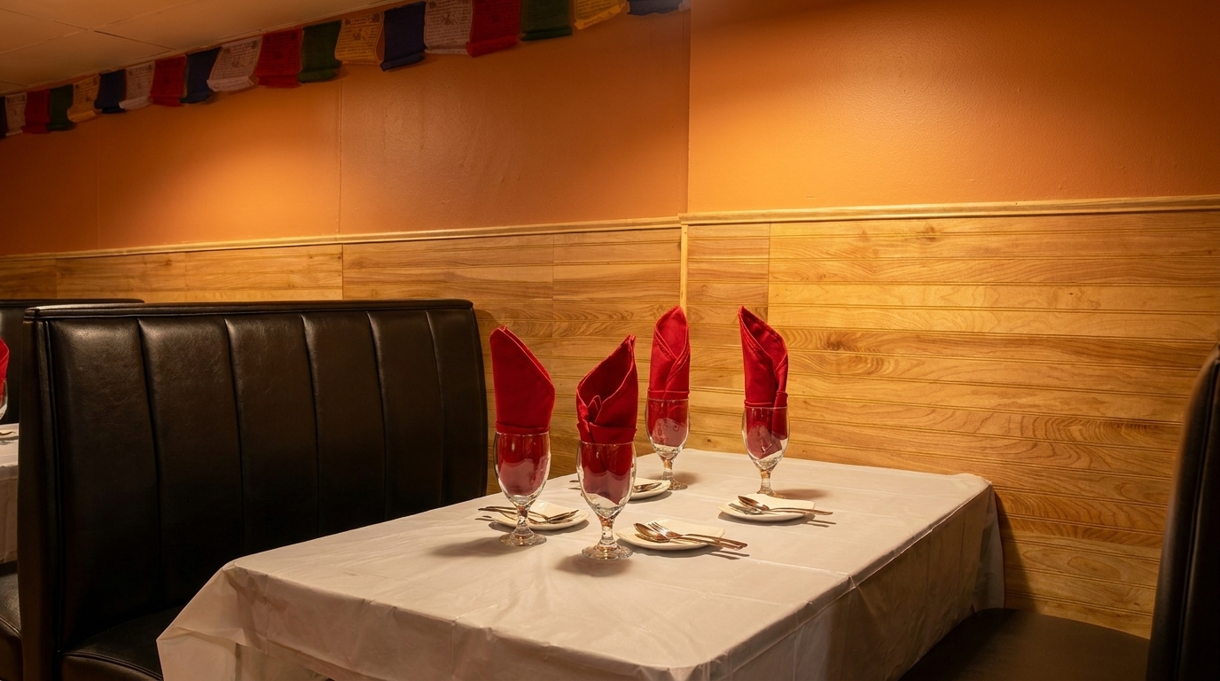 Restaurant booth with a set table, red napkins in glasses, and prayer flags overhead.