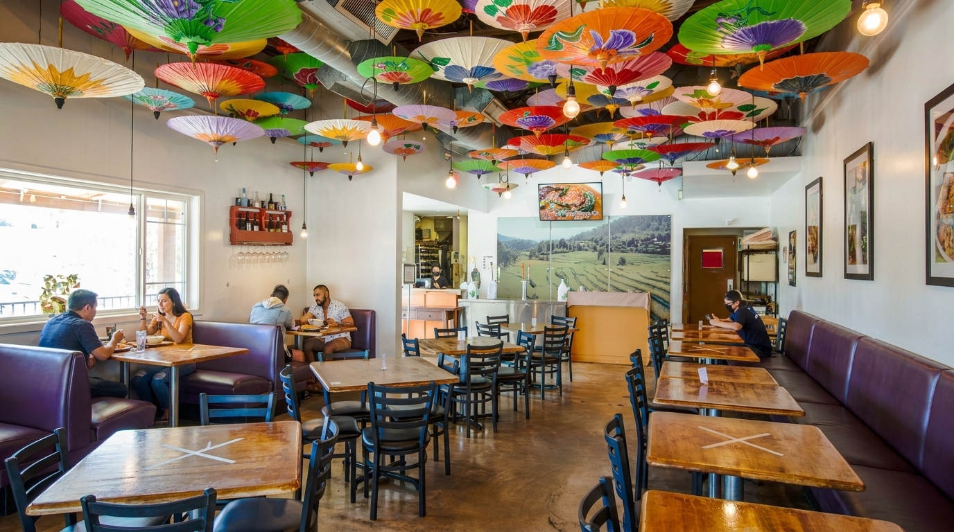 Restaurant interior with colorful paper umbrellas on the ceiling, diners at tables, and a large landscape mural.