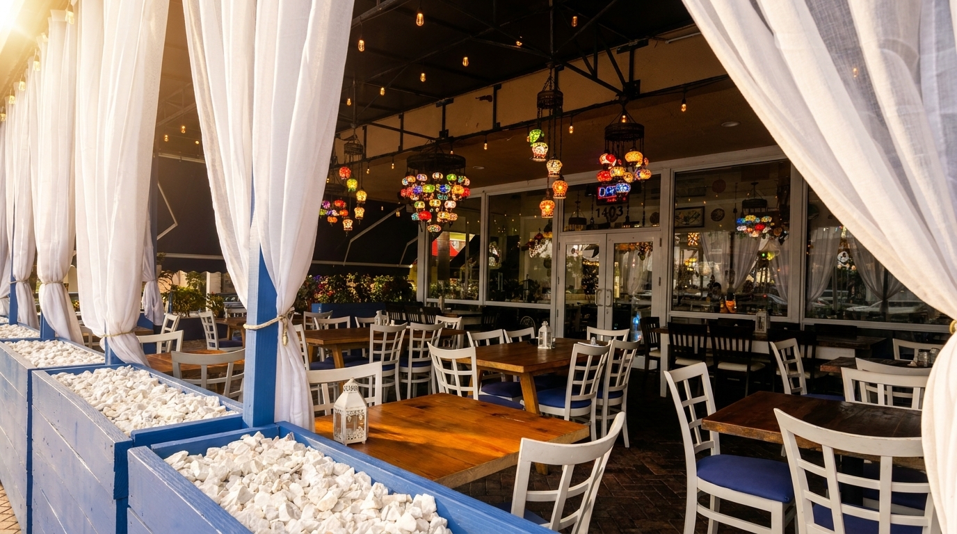 Outdoor patio dining area with white curtains, wooden tables, white chairs, and colorful hanging lamps.
