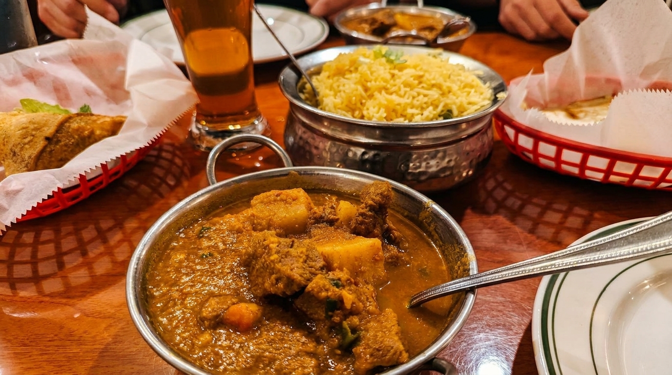 Indian dishes on a wooden table, including curry, rice, samosas, and naan.