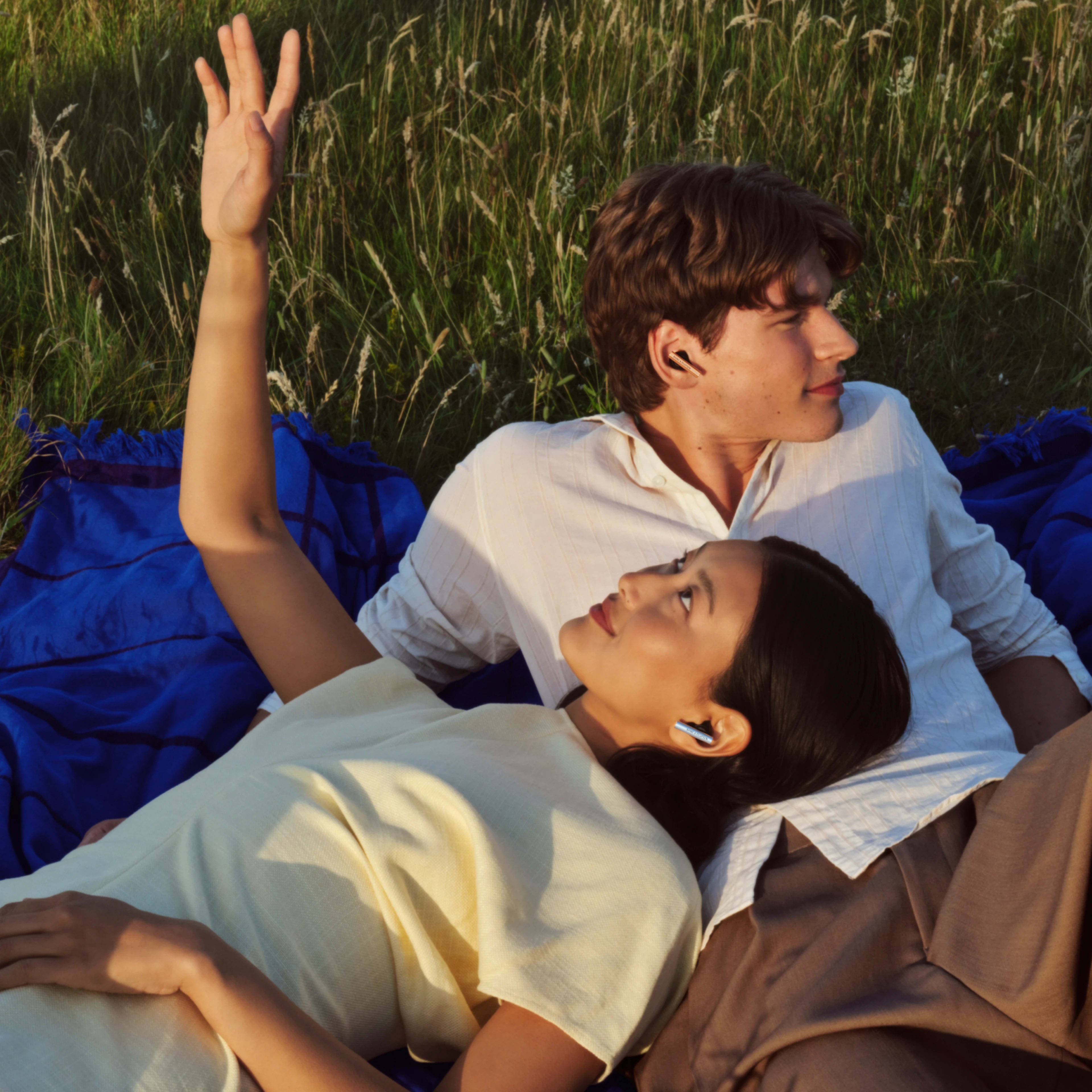 A couple lying down together on the grass wearing Super Hoodie earbuds and enjoying their time