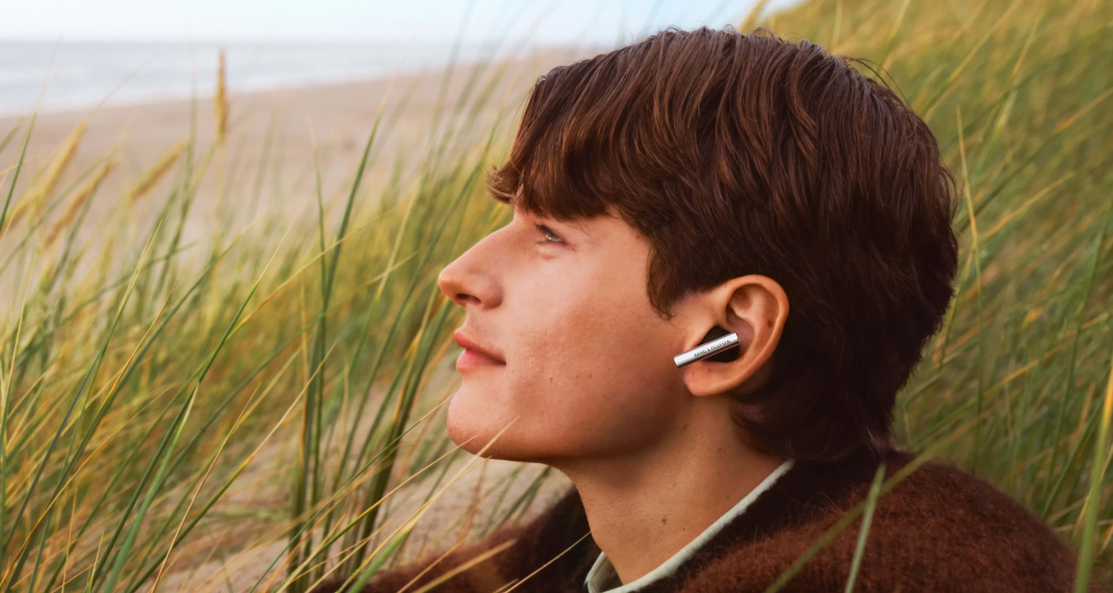 Side face of a man wearing Super Hoodie Aluminium color, sitting outside near the ocean gazing somewhere 