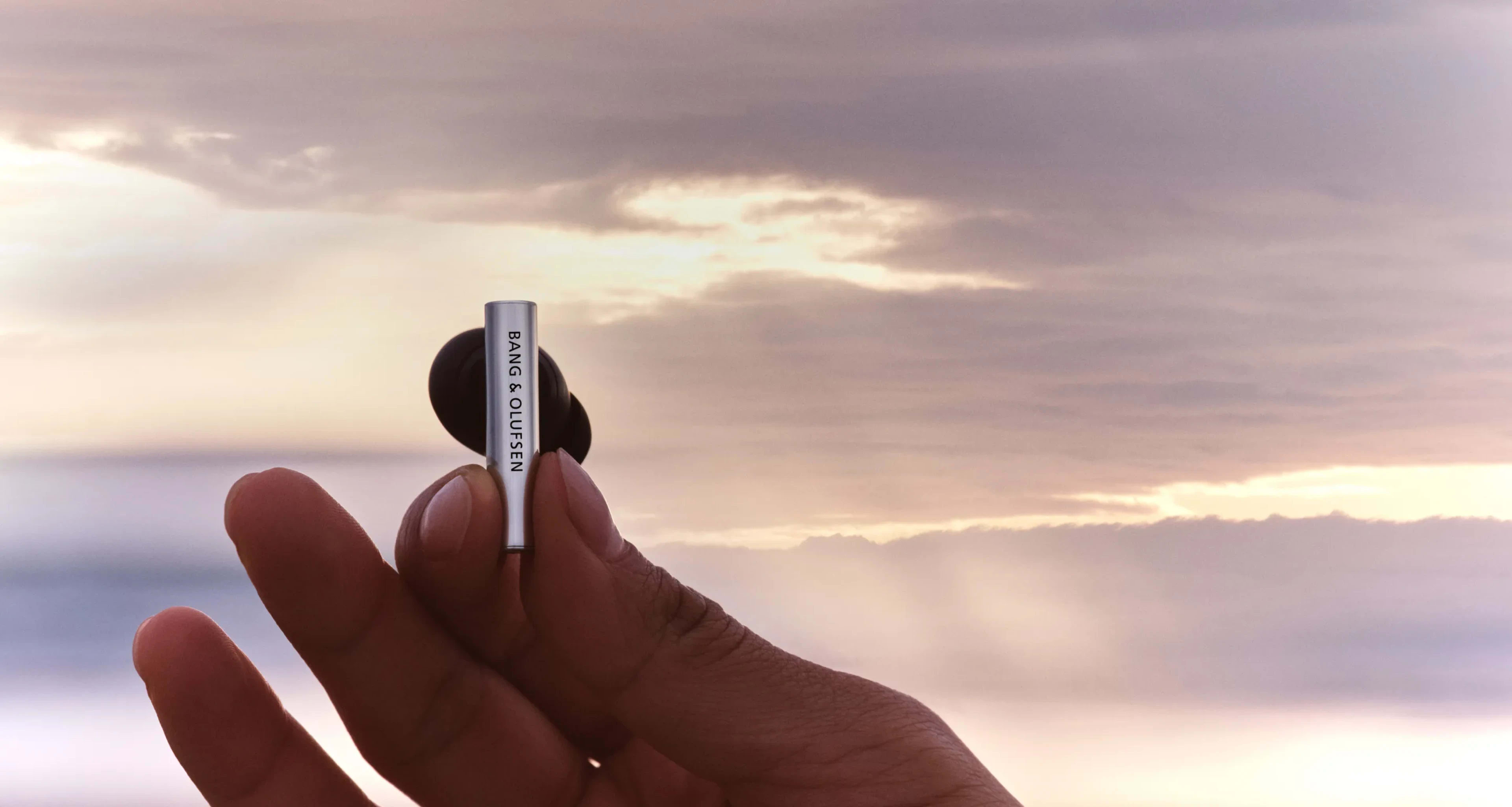 A hand holding one of Super Hoodie earphone piece with a beautiful sunset background behind