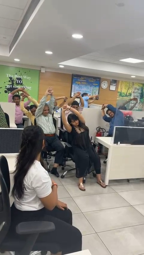 Corporate team performing desk stretches with arms raised during a guided office wellness session