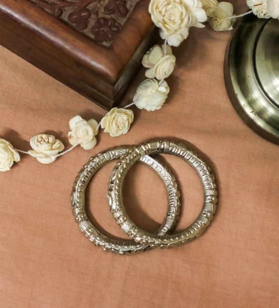 Pair of silver-toned Golap Bala bangles with full intricate traditional designs on a light brown background.