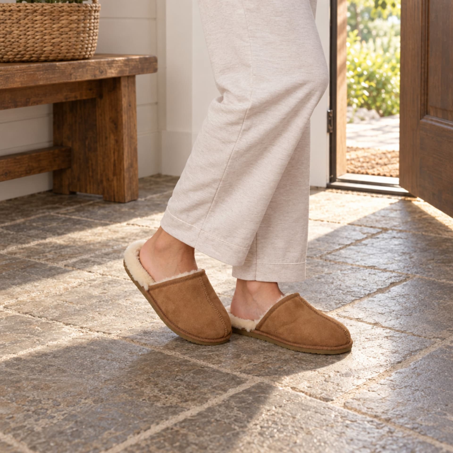 Brown suede sheepskin slippers worn with cream linen trousers in a warm interior
