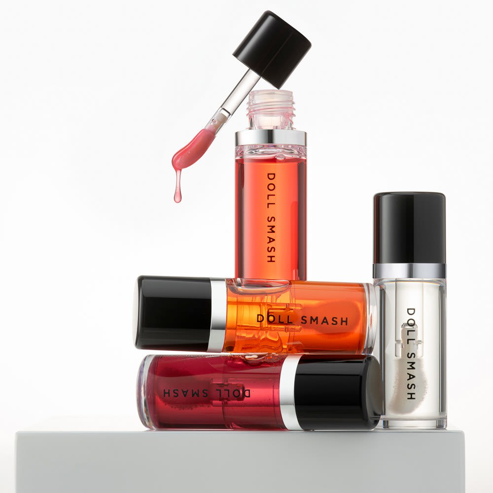 Doll Smash lip oils arranged together with an open applicator and a drop of gloss
