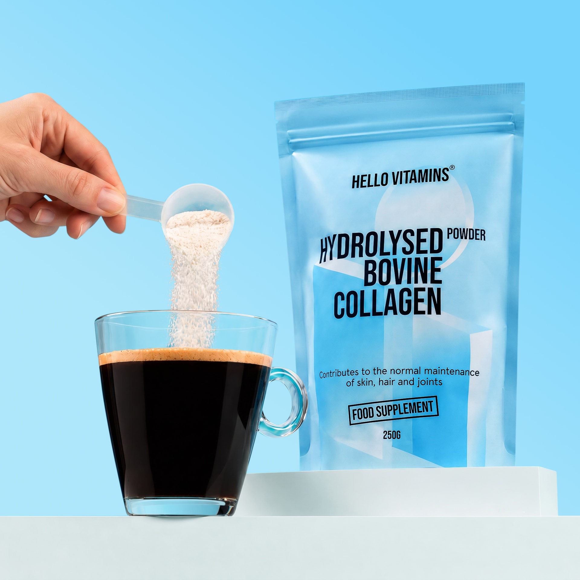 Hello Vitamins collagen powder being added to a glass of coffee on a blue set