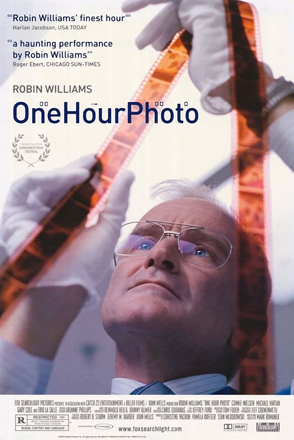 Alt text: Movie poster for 'One Hour Photo' featuring Robin Williams examining film negatives, highlighting themes of voyeurism.