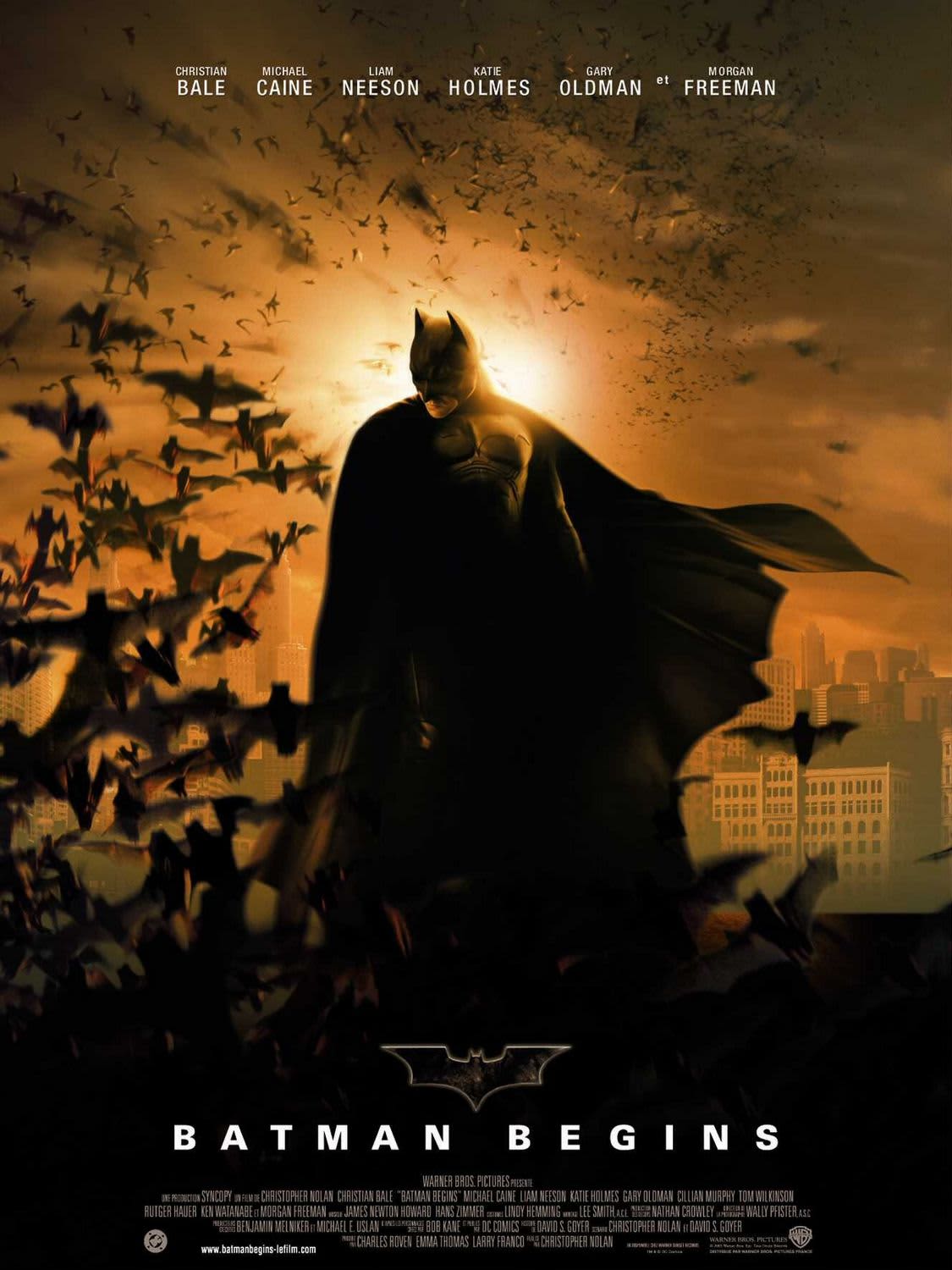 Batman stands silhouetted against a sunset, surrounded by bats, in the movie poster for Batman Begins.