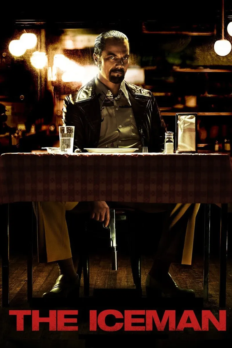 A man in a leather jacket sits at a table with a gun in his hand, representing themes of antisocial behavior in The Iceman.