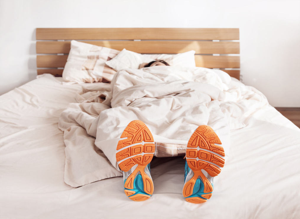 Runner's feet resting on bed, covered by a light blanket, symbolizing recovery and rest for peak performance.