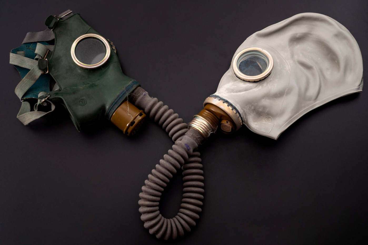 Two vintage gas masks positioned on a dark background, highlighting different styles and features of protective gear.