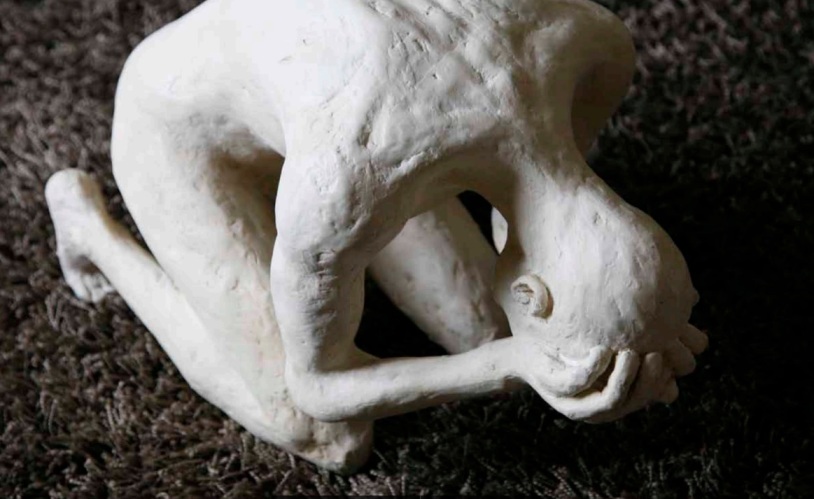 Sculpture of a person kneeling in a posture of grief, reflecting the emotional process of loss and healing.